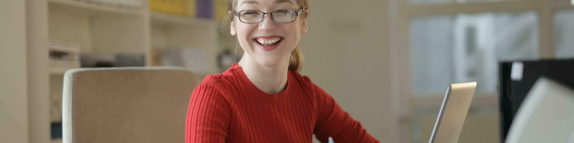 a woman in a red sweater smiling at her desk